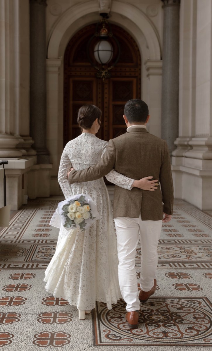 Bride and groom walk away arm in arm towards a carved timber door