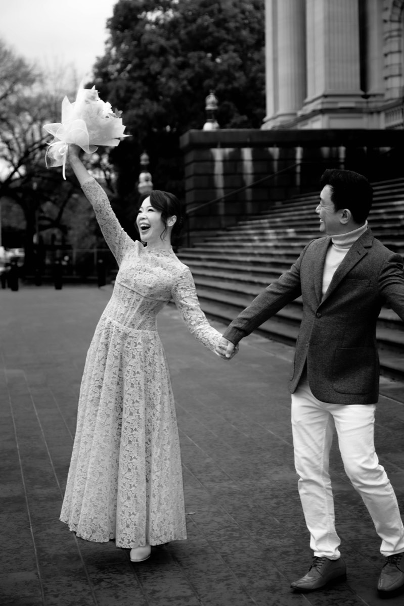 Black and white photo of the bride raising her bouquet in celebration on the steps, laughing
