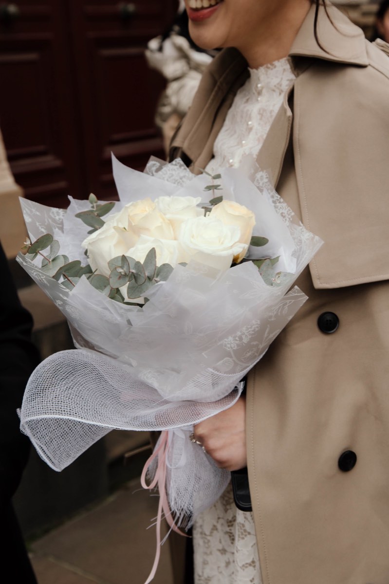 Detail of the white rose bouquet wrapped in tulle against a trench coat
